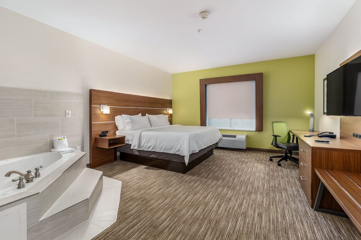 A modern hotel room with a large bed, a separate bathroom with a bathtub, a desk with a chair, and a television.