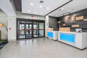 A hotel reception area with a glass door entrance, a reception desk, and a wall-mounted sign. - Holiday Inn Express Suites Van Buren-Ft Smith Area by IHG (Van Buren)
