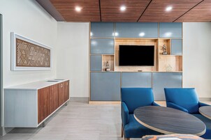 Un interior moderno con techo de madera, un televisor de pantalla plana montado en la pared, un sofá azul y un mueble de madera con símbolos de reciclaje.