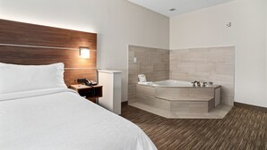 A modern hotel room with a large bed, a wooden headboard, a bedside table with a phone, a nightstand, and a bathroom with a bathtub and tiled walls. - Holiday Inn Express Suites Van Buren-Ft Smith Area by IHG (Van Buren)