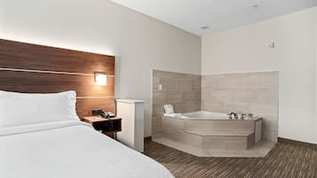 Una habitación de hotel moderna con una cama grande, cabecera de madera, mesita de noche con teléfono y un baño con bañera y paredes de azulejos.