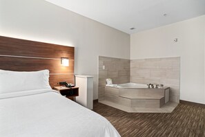 A modern hotel room with a large bed, a wooden headboard, a bedside table with a phone, a nightstand, and a bathroom with a bathtub and tiled walls. - Holiday Inn Express Suites Van Buren-Ft Smith Area by IHG (Van Buren)