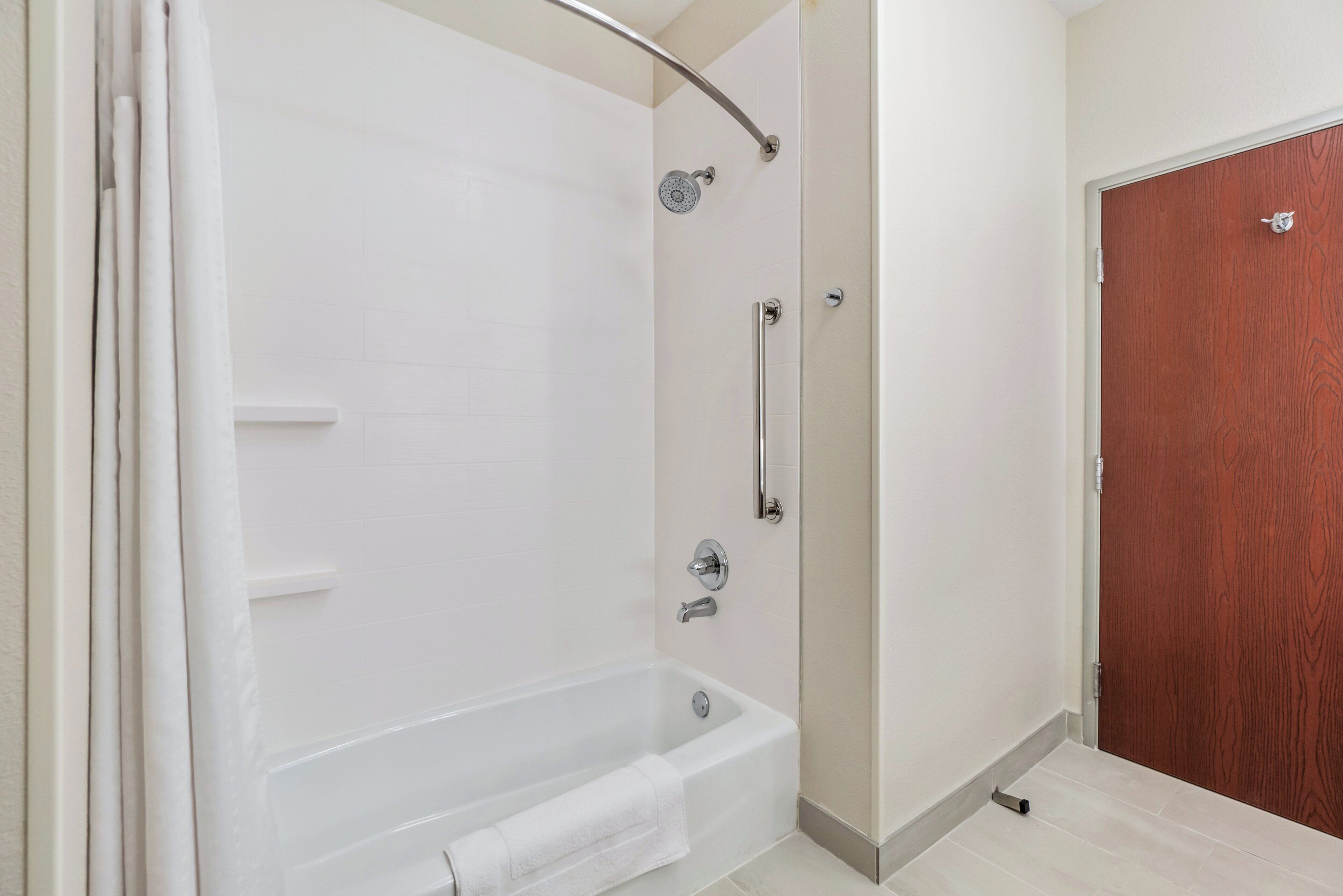 A modern bathroom with a walk-in shower, a bathtub, and a wooden door.