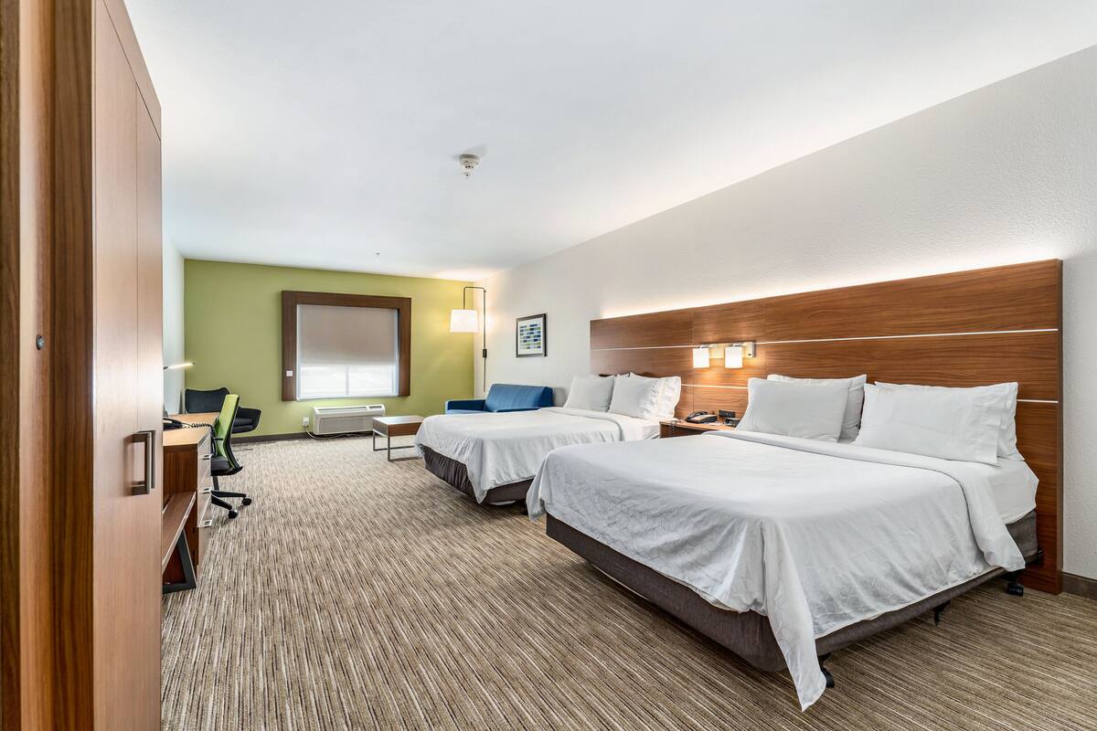 A hotel room with two beds, a desk, a chair, and a large window.