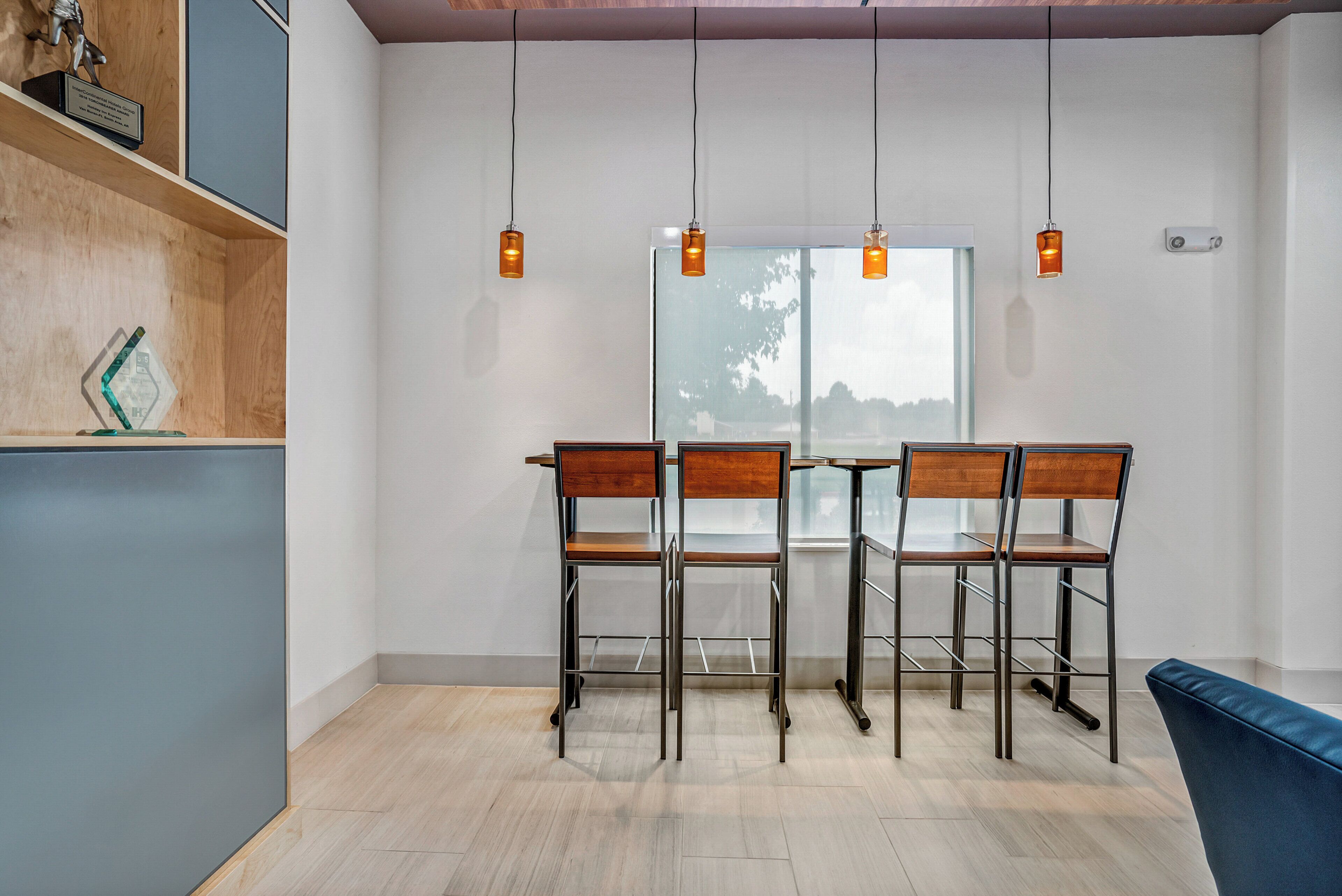 Un comedor moderno con una mesa y sillas de madera, vista a través de un ventanal e iluminación colgante.