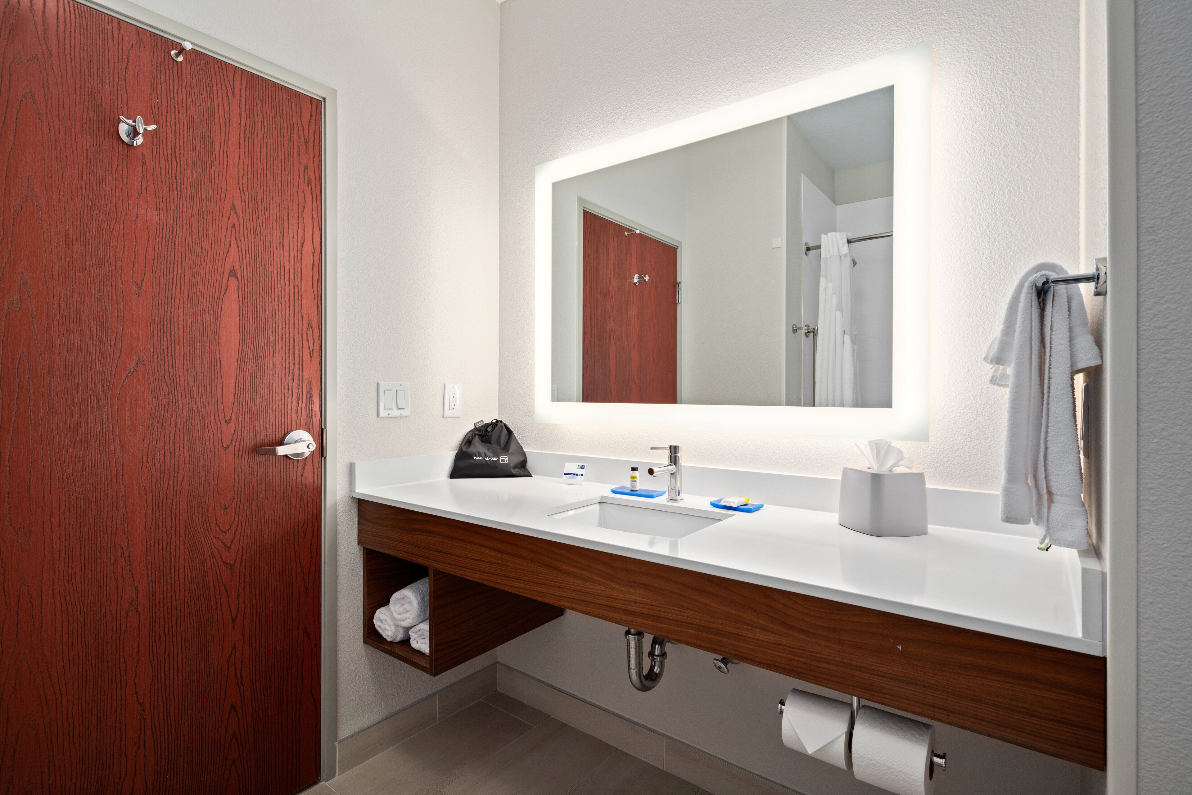 A modern bathroom with a wooden vanity, a large mirror, and a towel rack.