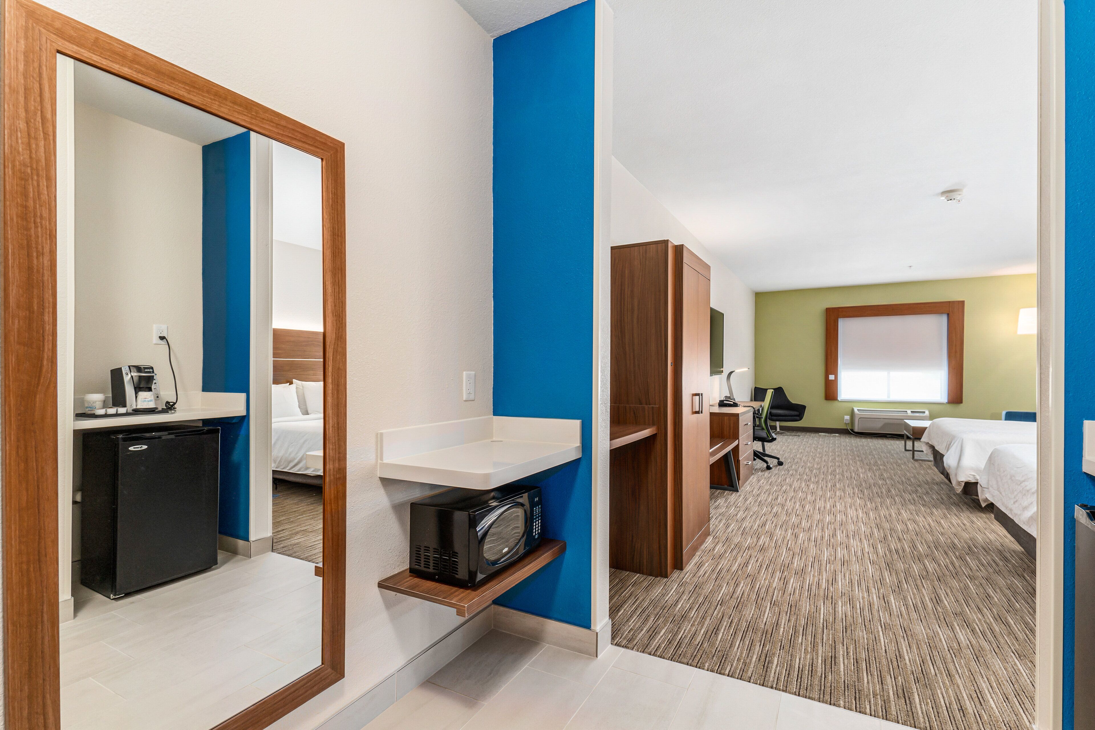 Une chambre d’hôtel équipée d’un lit, d’un bureau, d’une chaise, d’un four à micro-ondes, d’un réfrigérateur et d’une petite étagère.