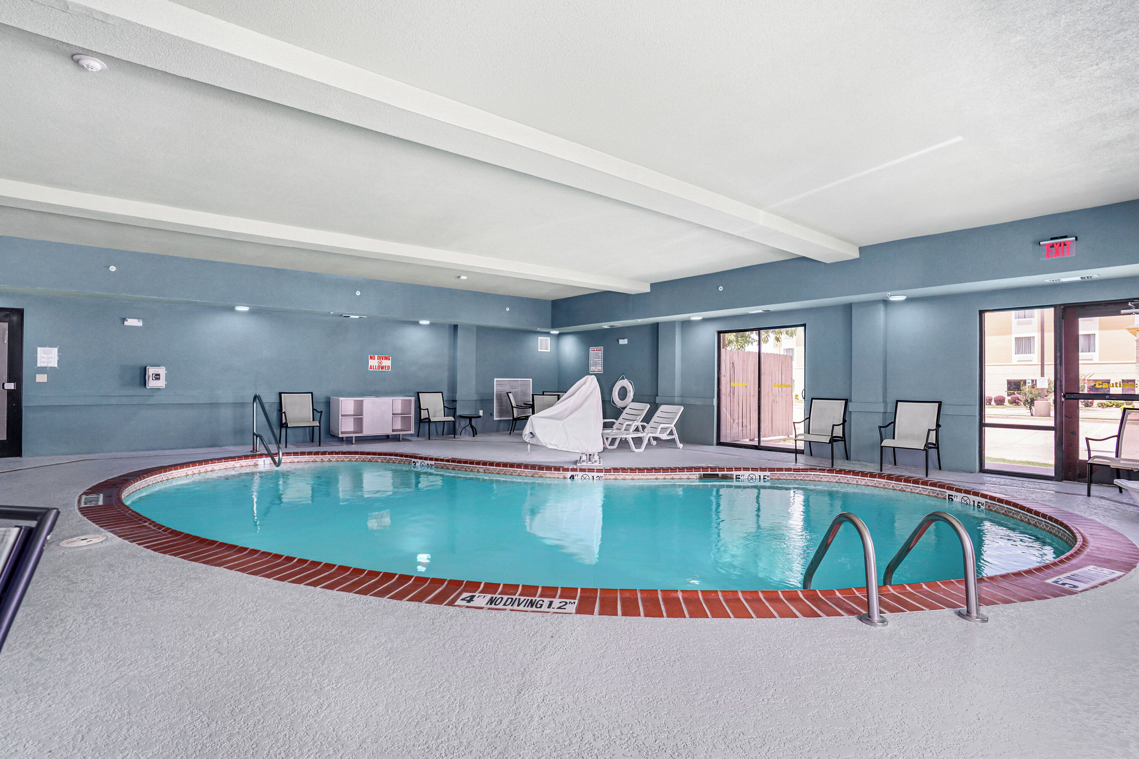 An indoor swimming pool with a diving board, lounge chairs, and a covered seating area.