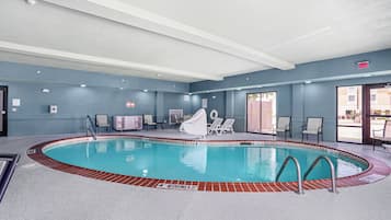 An indoor swimming pool with a diving board, lounge chairs, and a covered seating area.