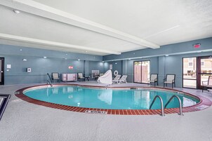Una piscina interior con trampolín, sillas de descanso y una zona de estar cubierta.