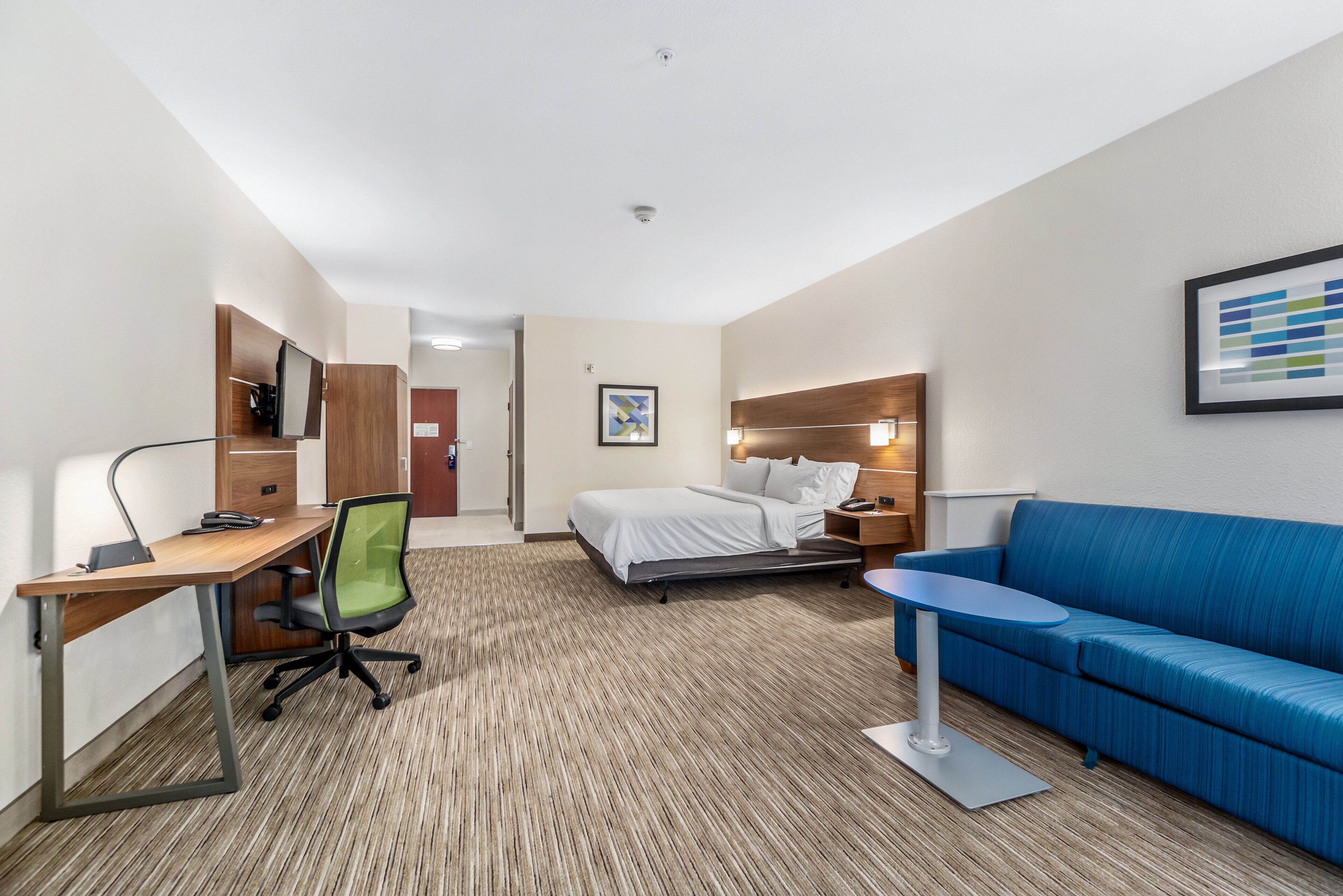 A hotel room with a bed, a desk with a chair, a blue sofa, and a small table.