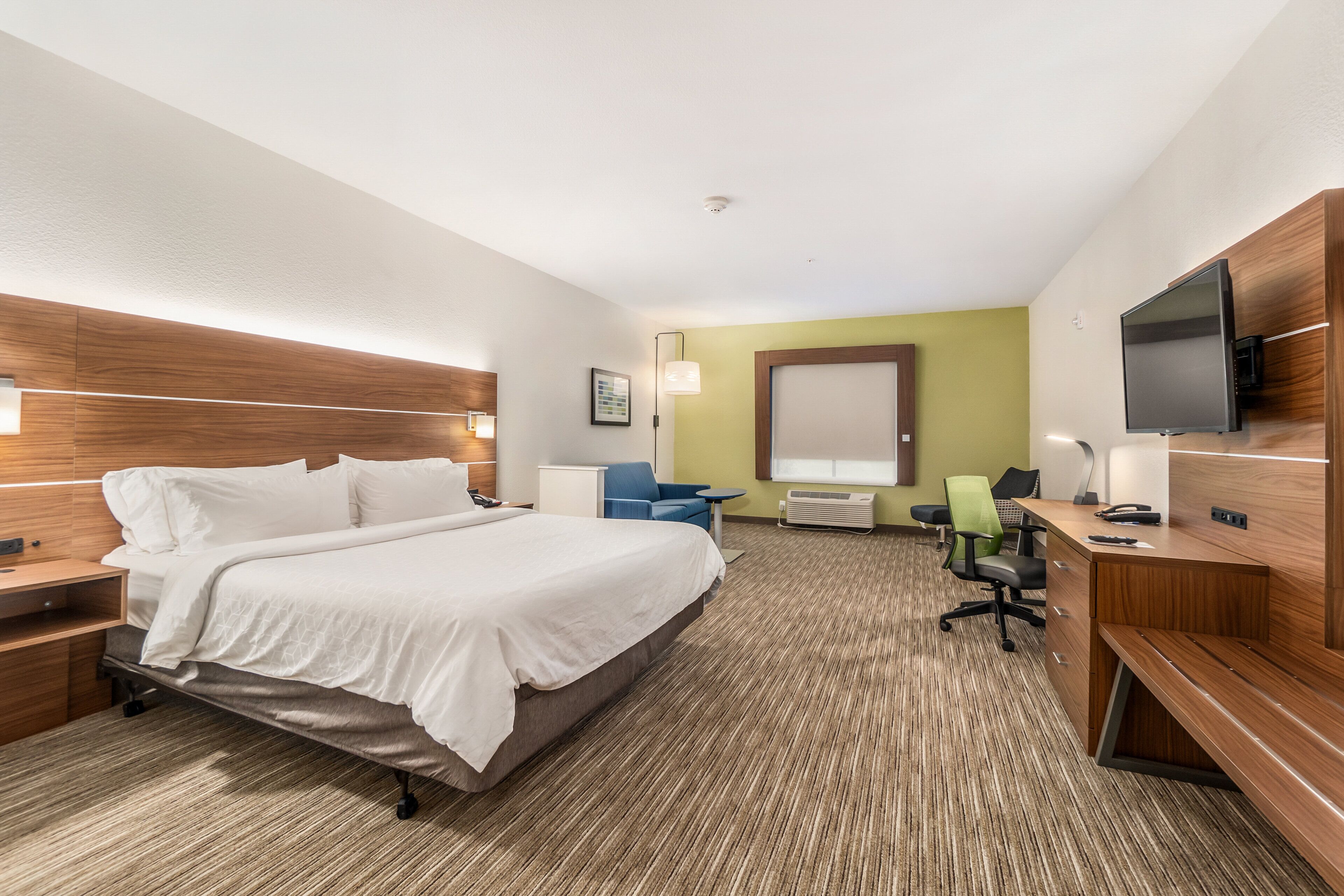 Habitación de hotel con una cama grande, un escritorio con computadora, un televisor y una silla.