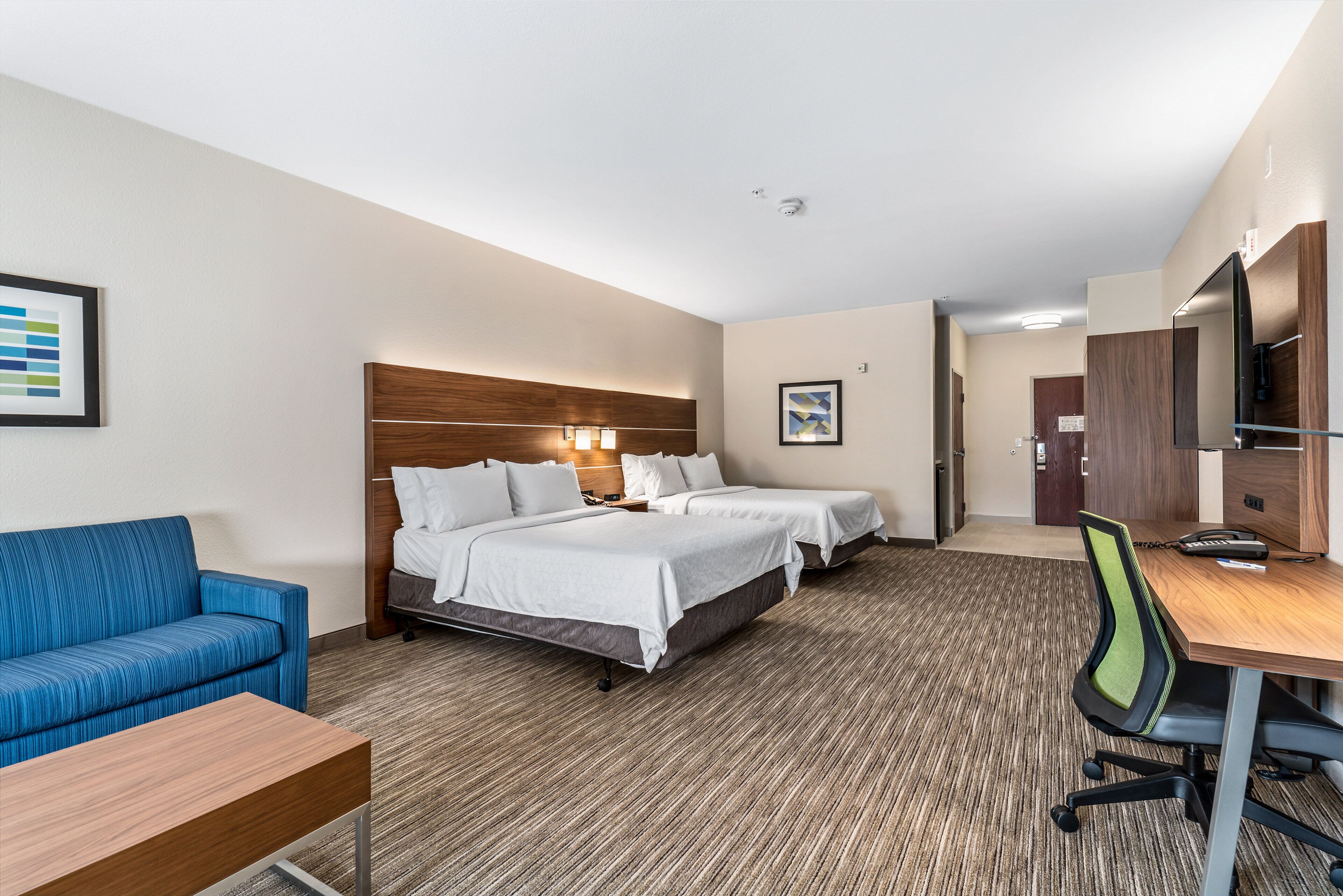 A hotel room with two beds, a desk, a chair, a sofa, and a TV.