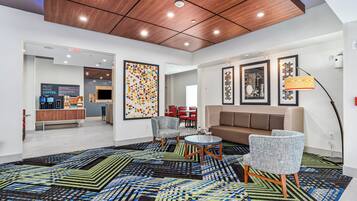 Un lobby moderno con techo de madera, una estación de café, una zona de estar con sofá y sillones, y una alfombra estampada.