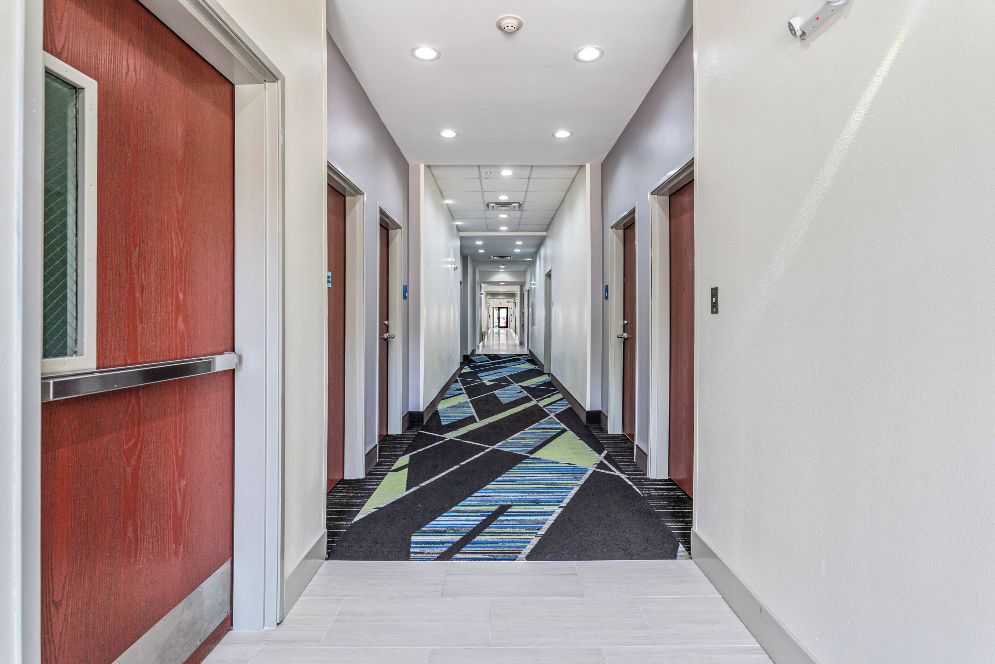 Un pasillo de hotel con alfombra estampada, puertas a ambos lados y un techo con iluminación empotrada.