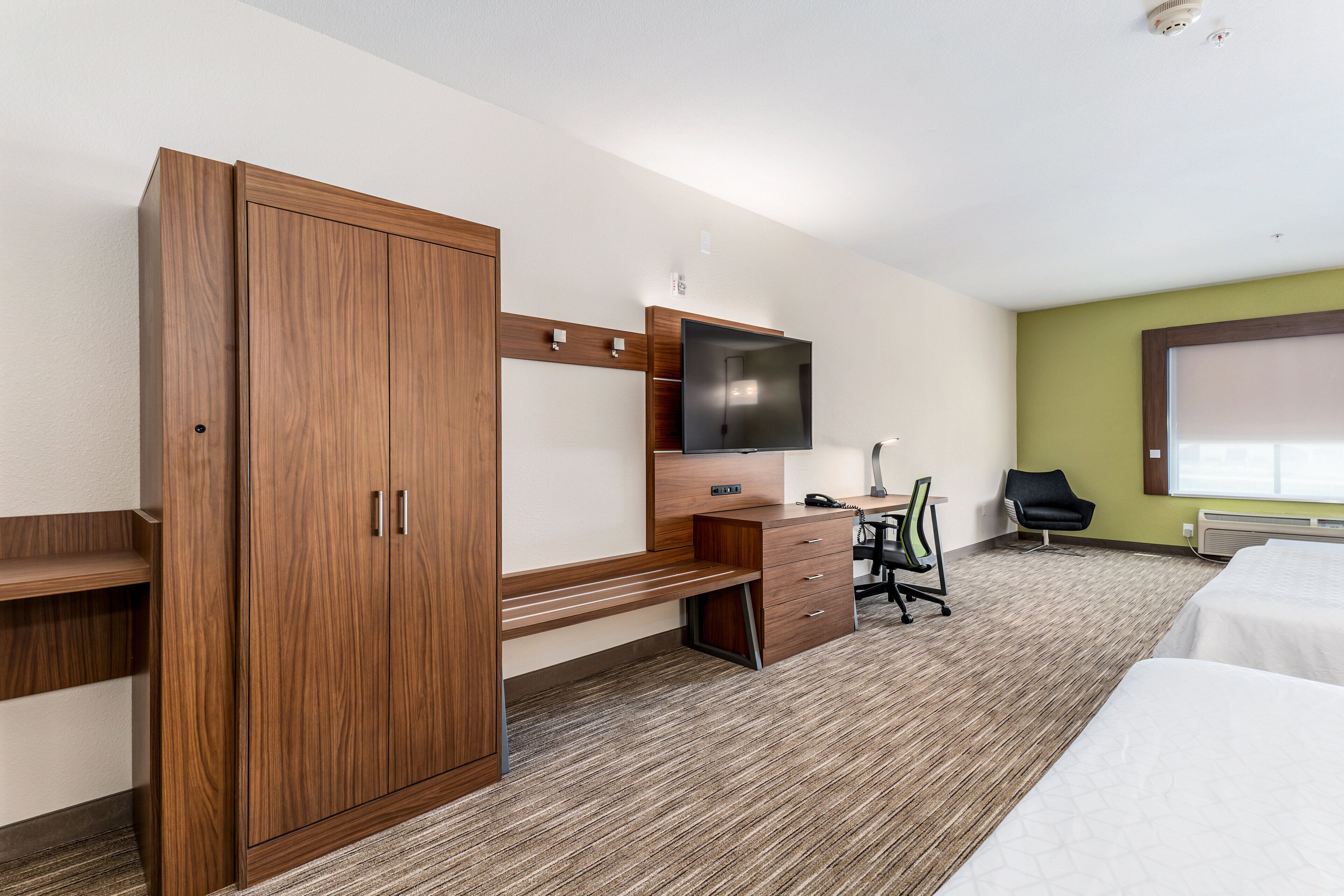 Une chambre d’hôtel avec une armoire en bois, un bureau doté d’un téléviseur à écran plat, une chaise et un lit.