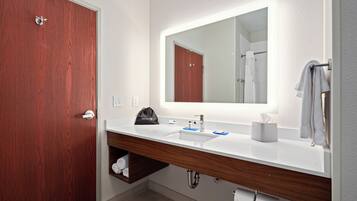 Un baño moderno con puerta de madera, un lavabo blanco, un espejo con luz y un perchero para toallas.