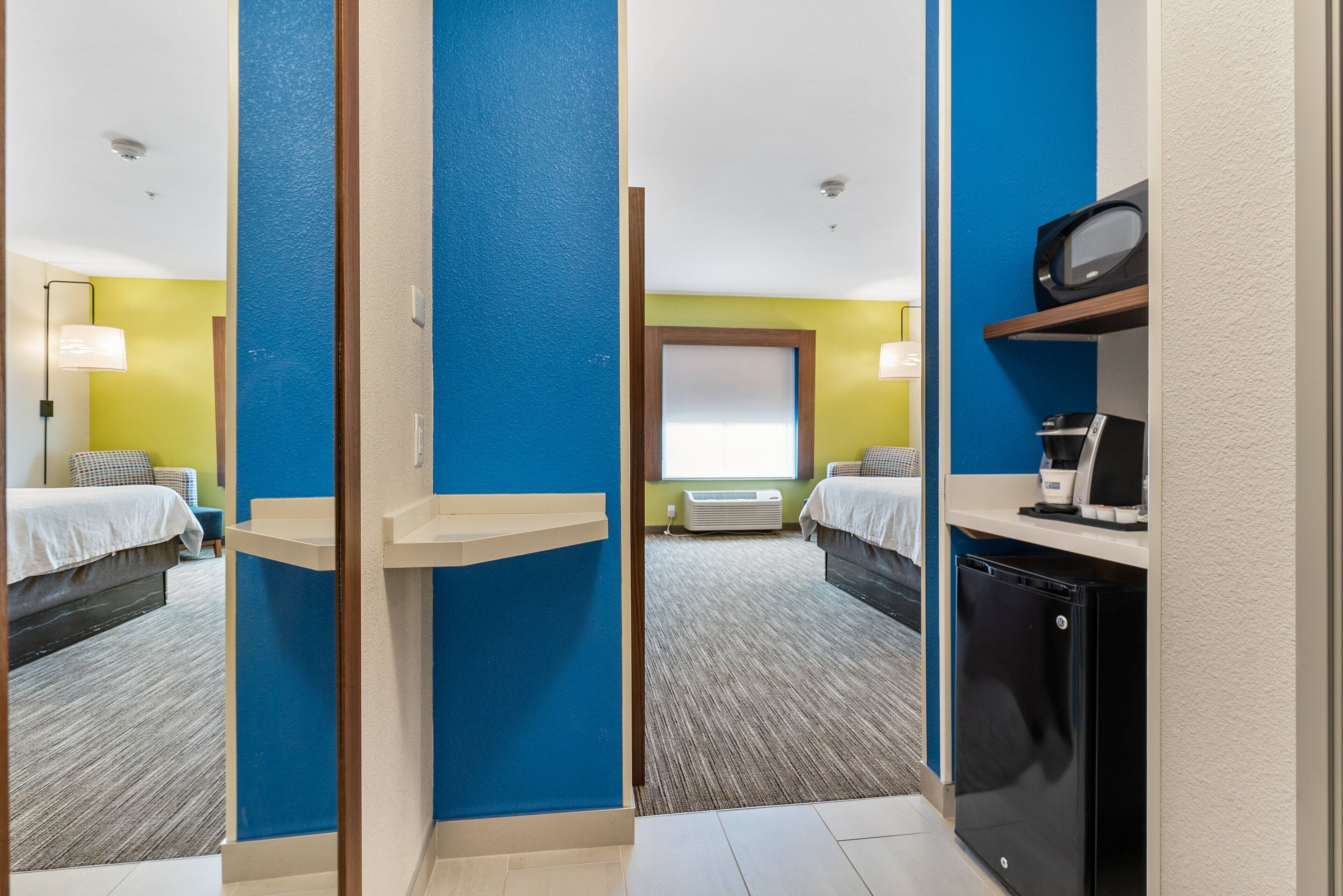 A hotel room with two beds, a microwave, a coffee maker, and a small refrigerator.