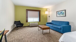 A hotel room with a green wall, a blue sofa, a wooden table, a black chair, and a framed picture on the wall. - Holiday Inn Express Suites Van Buren-Ft Smith Area by IHG (Van Buren)