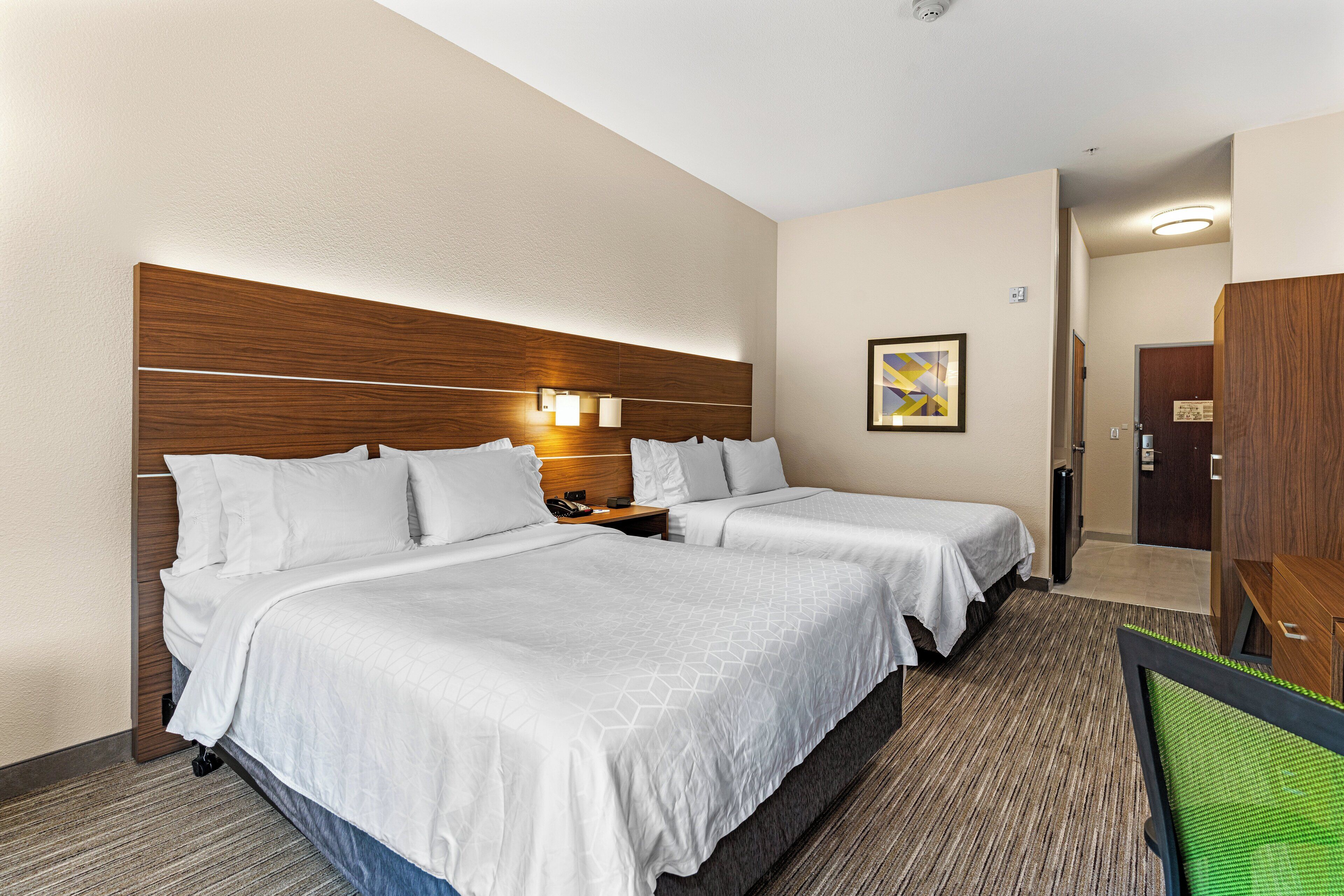 A hotel room with two beds, a wooden headboard, a nightstand, and a wall-mounted light fixture.