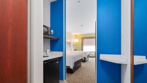 A hotel room with a compact layout, including a bed, bedside tables, a desk, and a compact kitchenette. - Holiday Inn Express Suites Van Buren-Ft Smith Area by IHG (Van Buren)