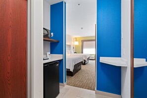 A hotel room with a compact layout, including a bed, bedside tables, a desk, and a compact kitchenette. - Holiday Inn Express Suites Van Buren-Ft Smith Area by IHG (Van Buren)
