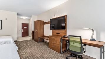 A hotel room with a bed, a desk with a computer, a chair, a TV, and a lamp.