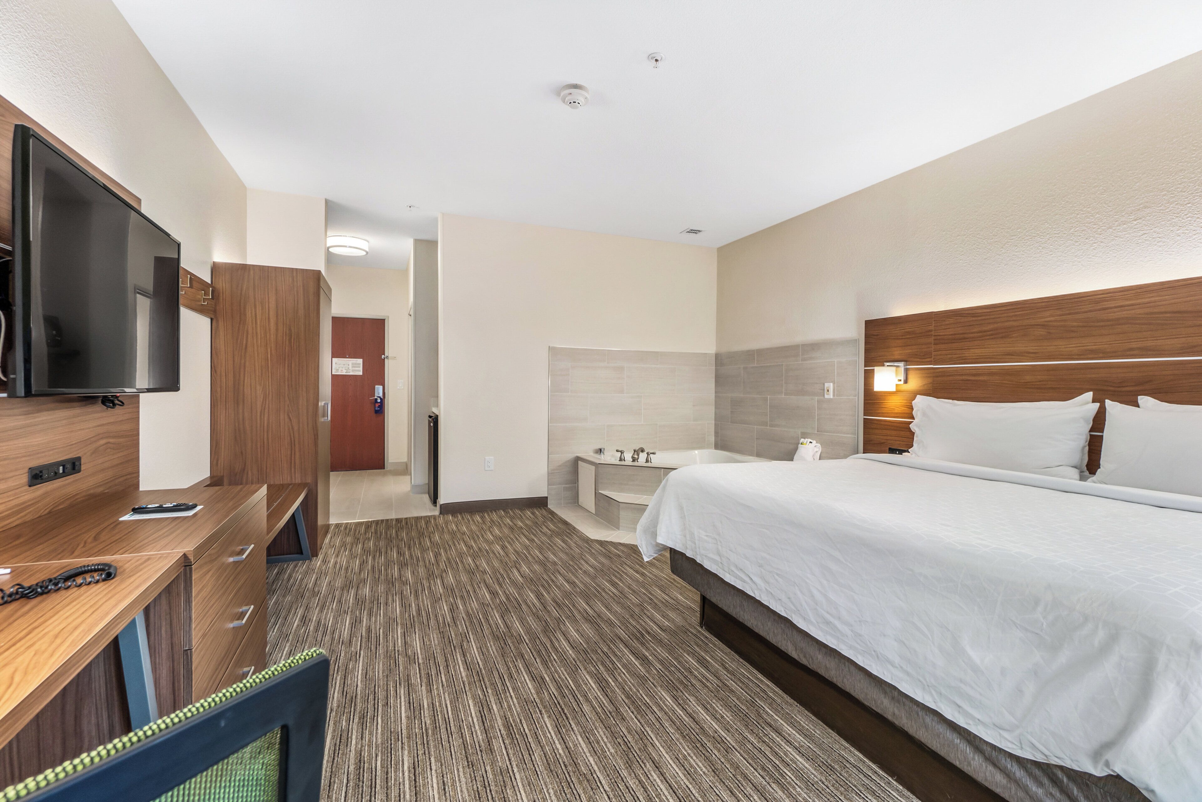 Habitación de hotel con cama, escritorio con televisor, baño y cabecero de madera.