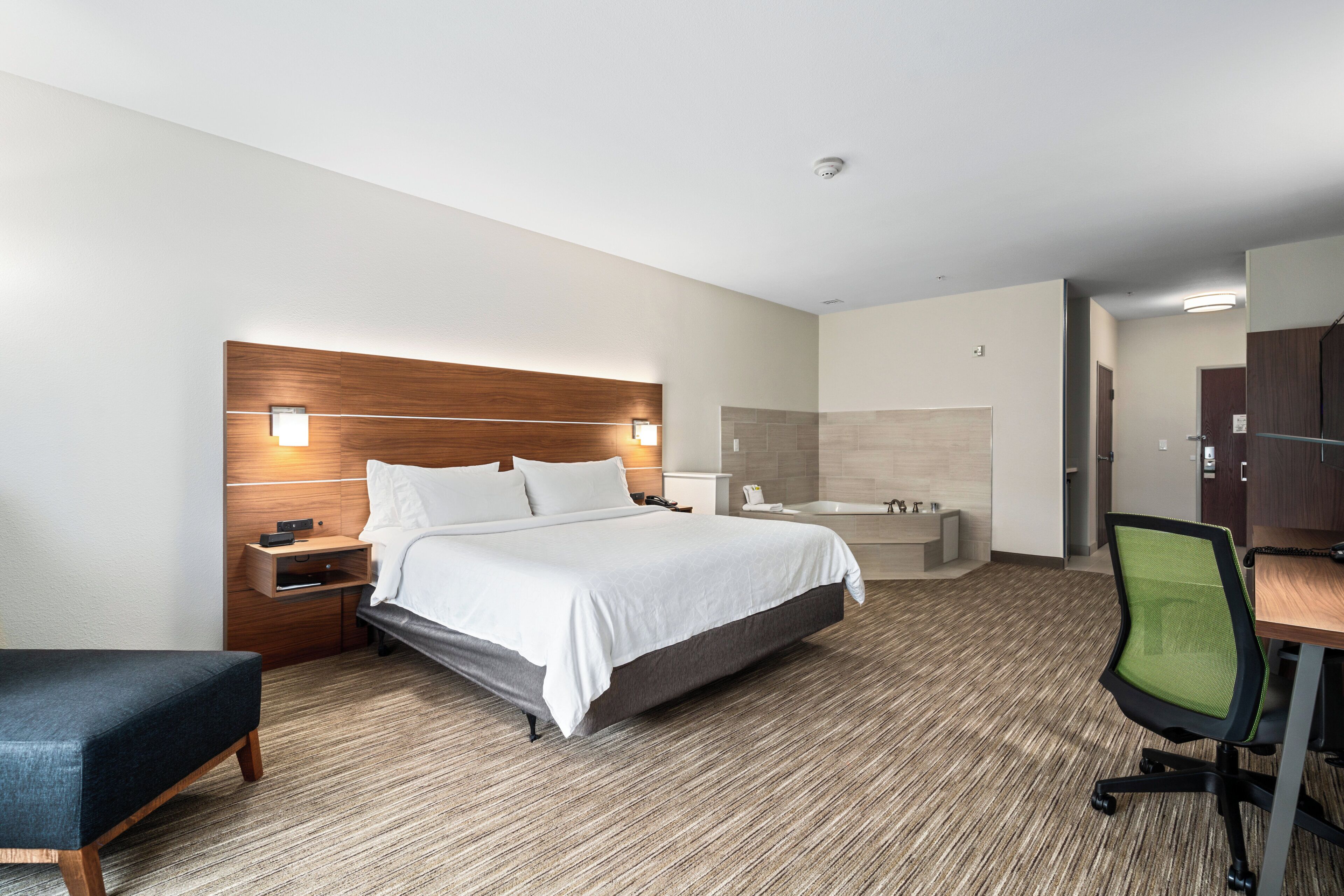 A hotel room with a bed, bedside table, chair, and a bathroom with a bathtub and shower.