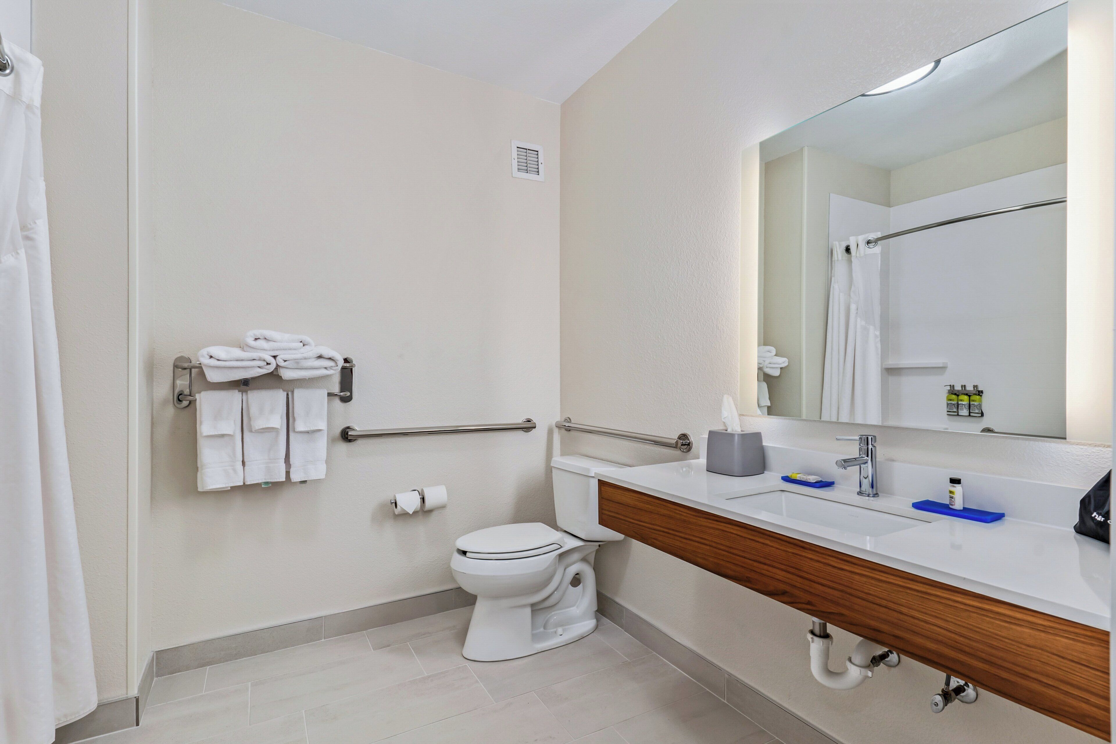 Un baño moderno con inodoro, lavamanos, espejo, toallero y cortina de ducha.