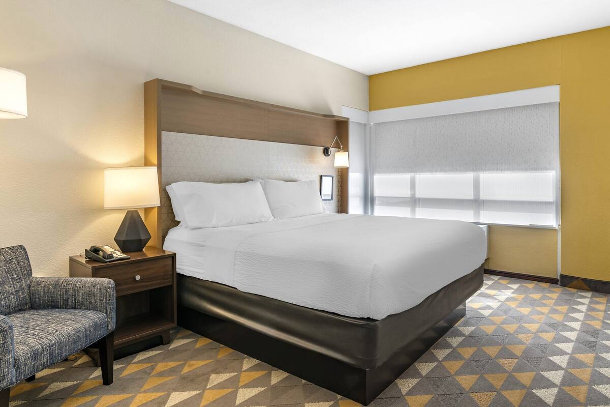 Une chambre d’hôtel avec un grand lit, une table de chevet avec une lampe, une chaise et un sol à motifs.