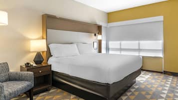 A hotel room with a large bed, a nightstand with a lamp, a chair, and a patterned floor.