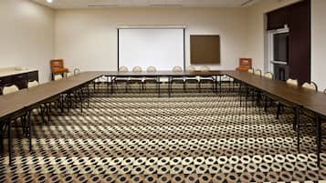 Une salle de conférence avec une longue table, des chaises, un écran de projection et une moquette à motifs.