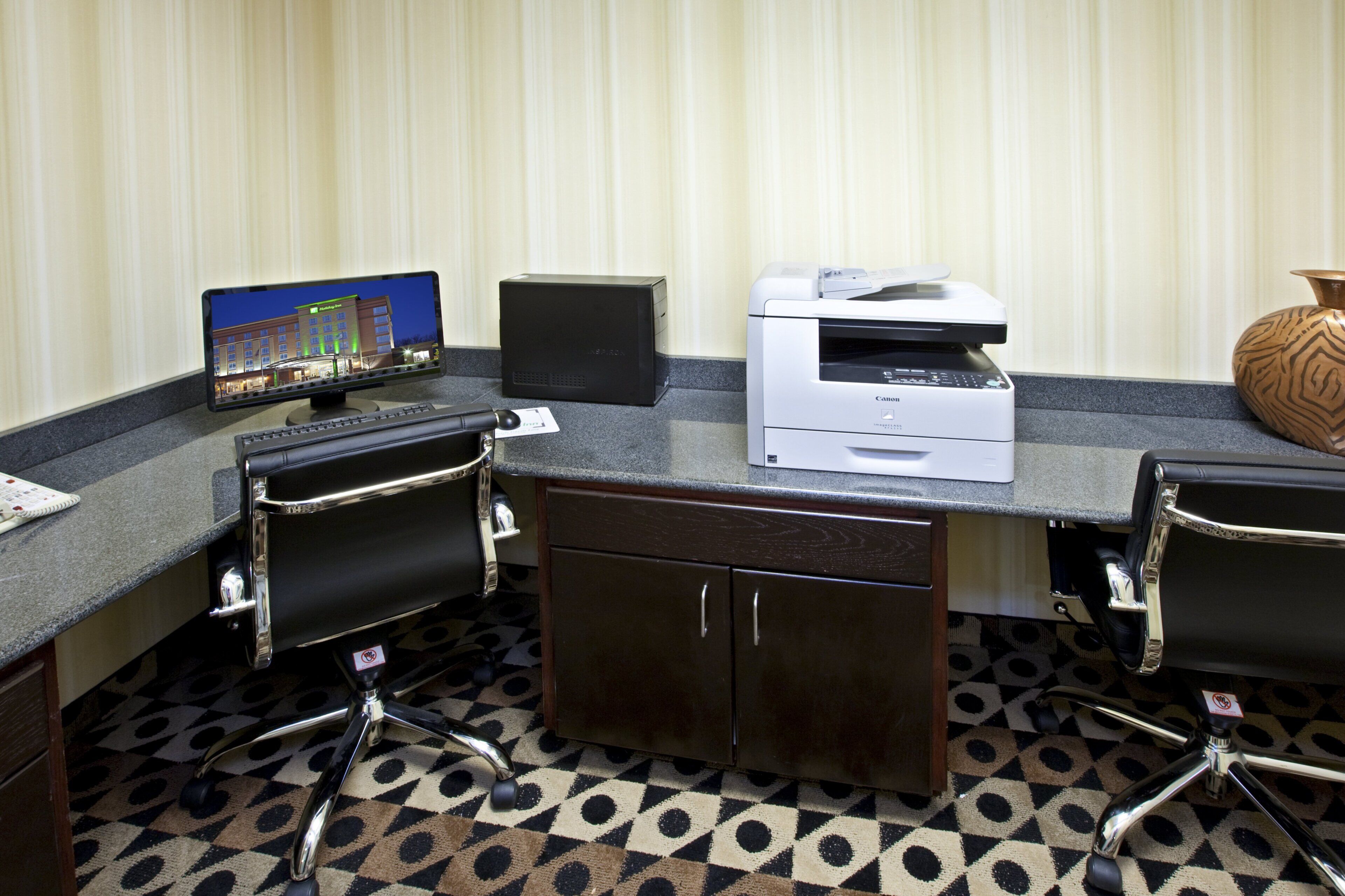 Een hotelconferentieruimte met een bureaudcomputer, een printer en een monitor waarop een afbeelding van een hotelgebouw te zien is.