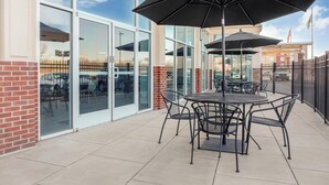 Une terrasse extérieure avec une table et des chaises, de grands parasols et une vue sur un bâtiment doté de portes vitrées.
