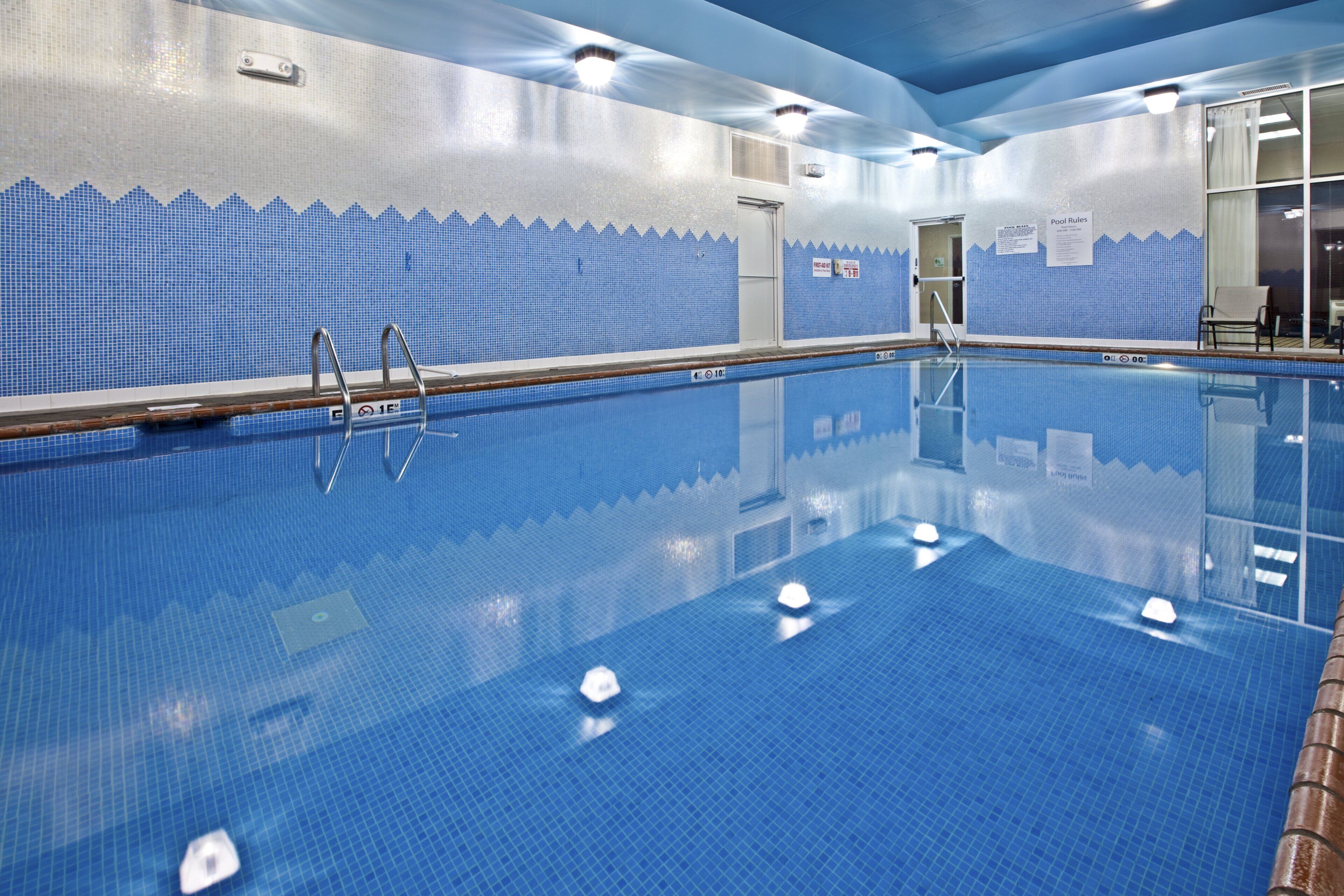 Una piscina interior con agua cristalina, paredes de azulejos y una escalera.