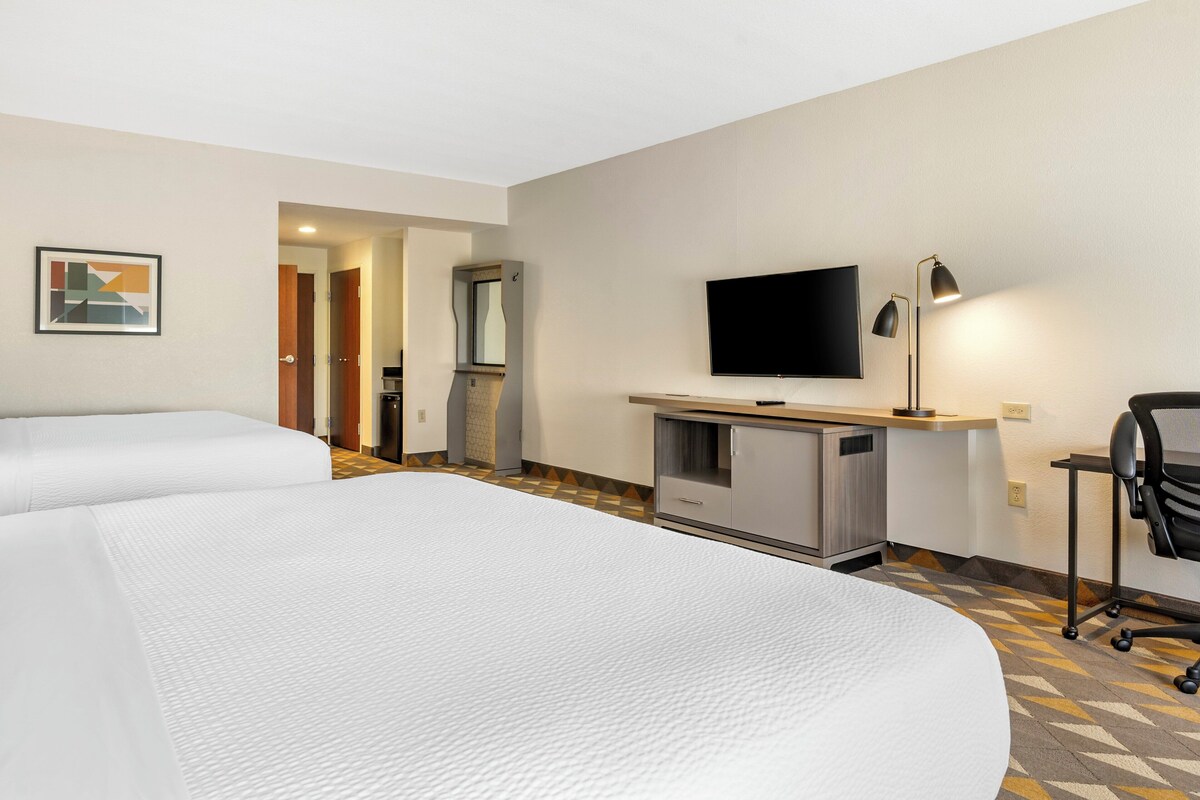 Une chambre d’hôtel avec deux lits, un bureau doté d’un téléviseur à écran plat, une lampe et une chaise.