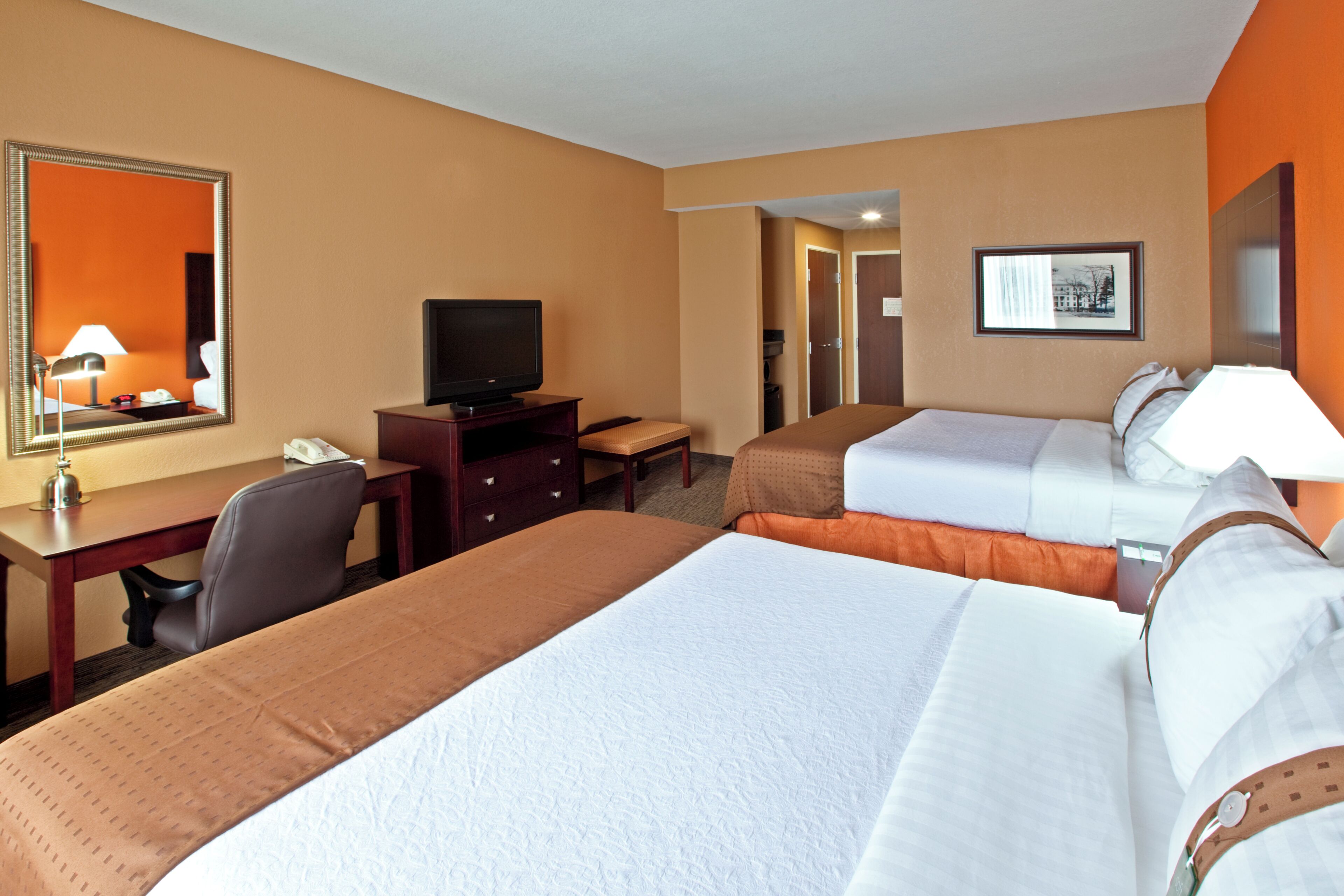 Una habitación de hotel con dos camas, un escritorio, un televisor y un espejo.