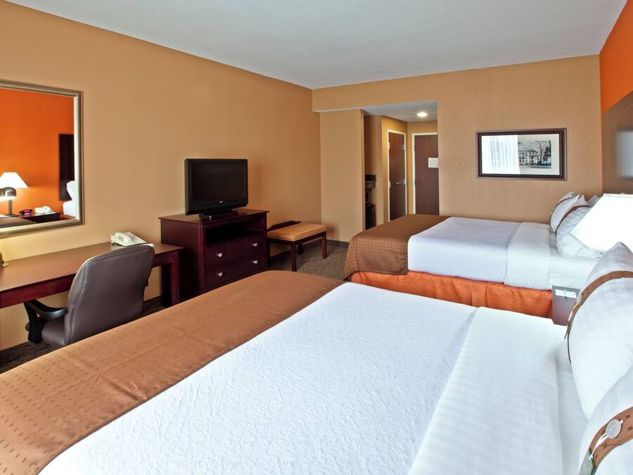 Una habitación de hotel con dos camas, un escritorio, un televisor y un espejo.