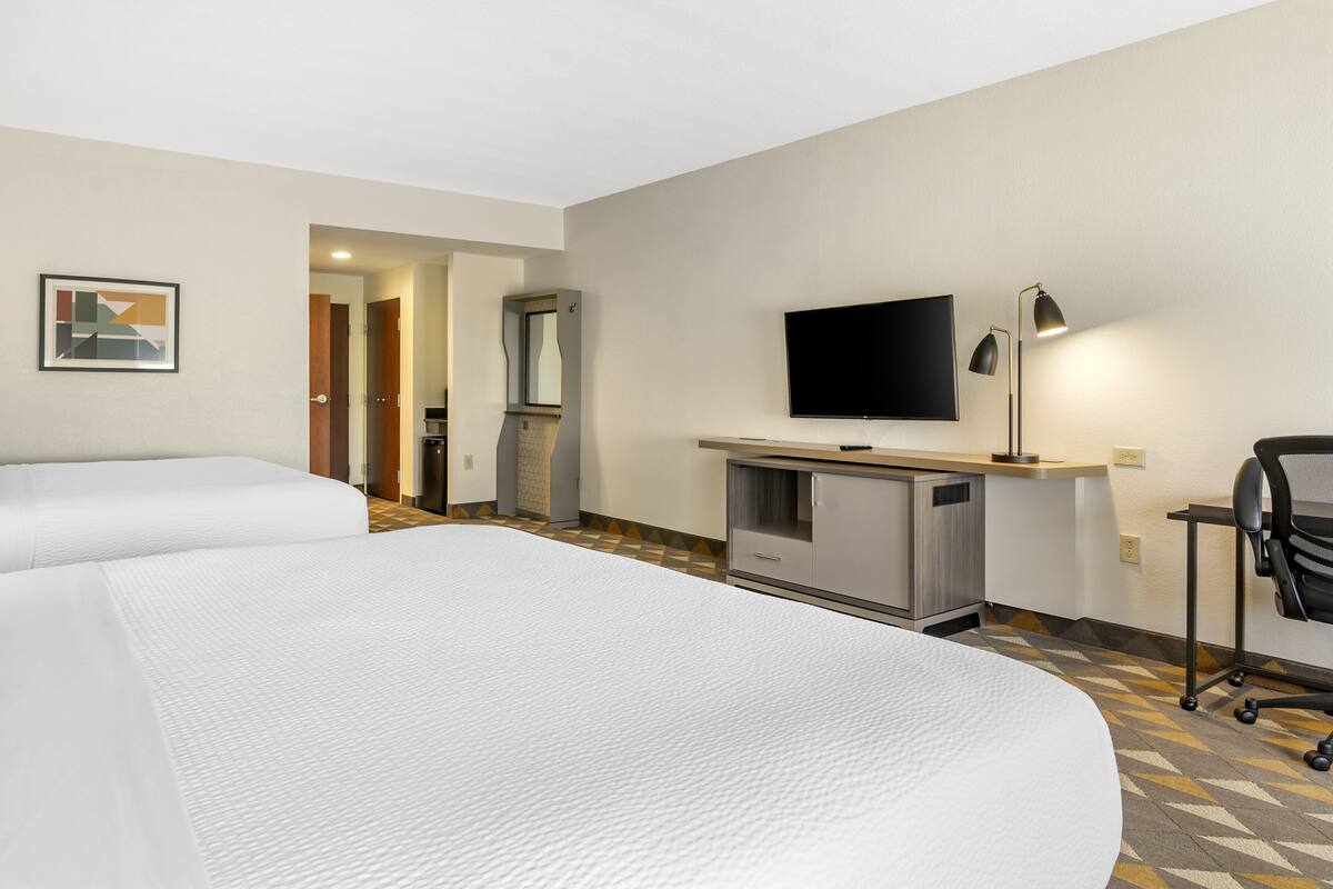 Une chambre d’hôtel avec deux lits, un bureau doté d’un téléviseur à écran plat, une lampe et une chaise.