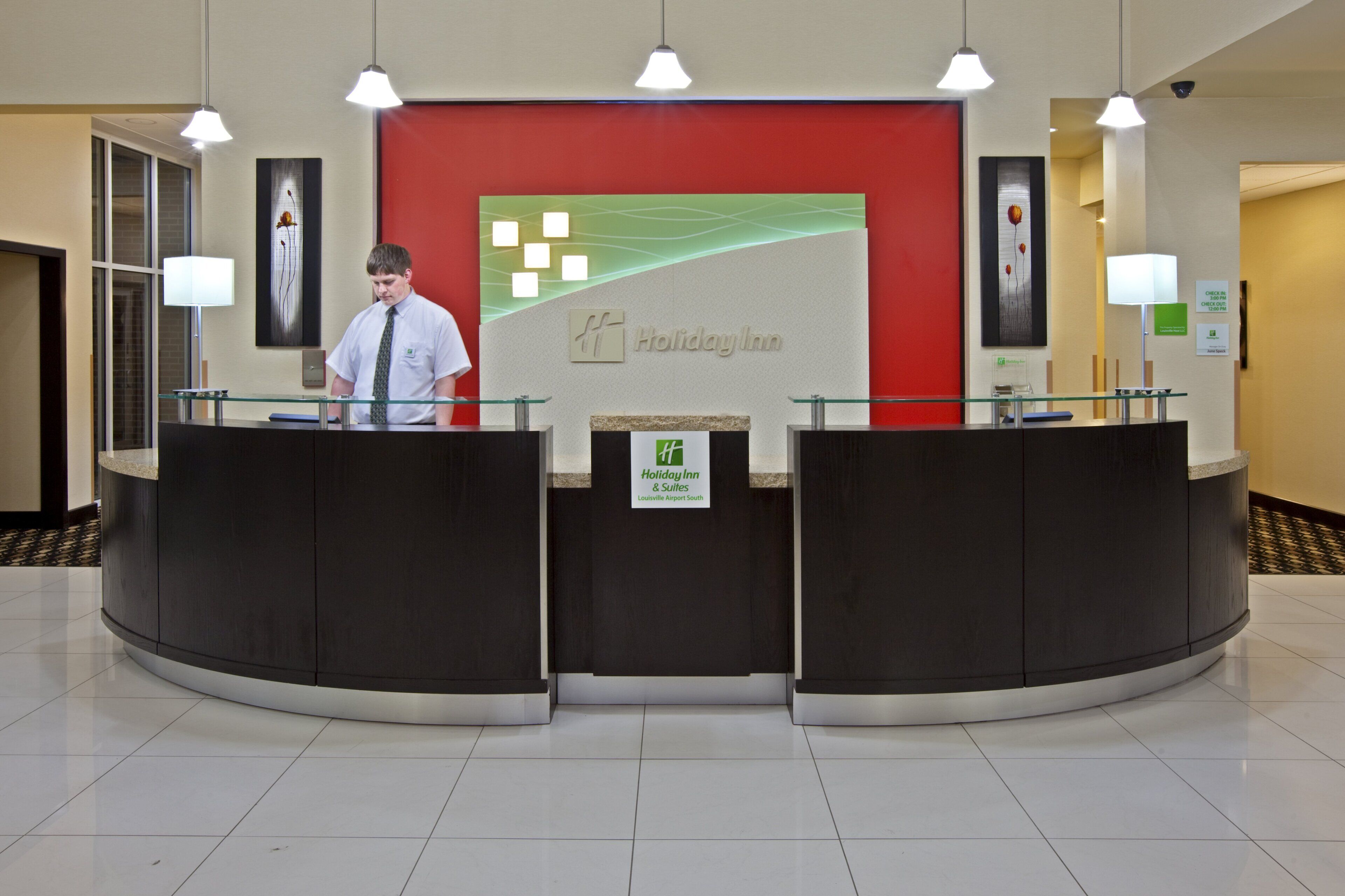 A reception desk at Holiday Inn with a modern design, featuring two glass partitions and a red accent wall.
