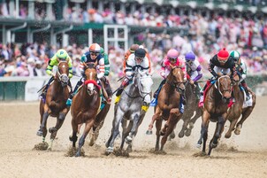 Una carrera de caballos con jinetes, una multitud de fondo y una pista de tierra.