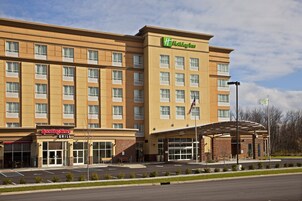 Un hotel Holiday Inn con entrada de ladrillo, zona de estacionamiento techada y una bandera estadounidense visible.