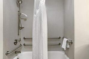Ein Badezimmer mit Badewanne, Haltegriffen, Duschkopf und Handtuchhalter.