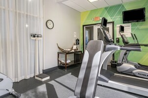 Un gimnasio con cintas de correr, un reloj de pared, una balanza y una cesta en un estante.