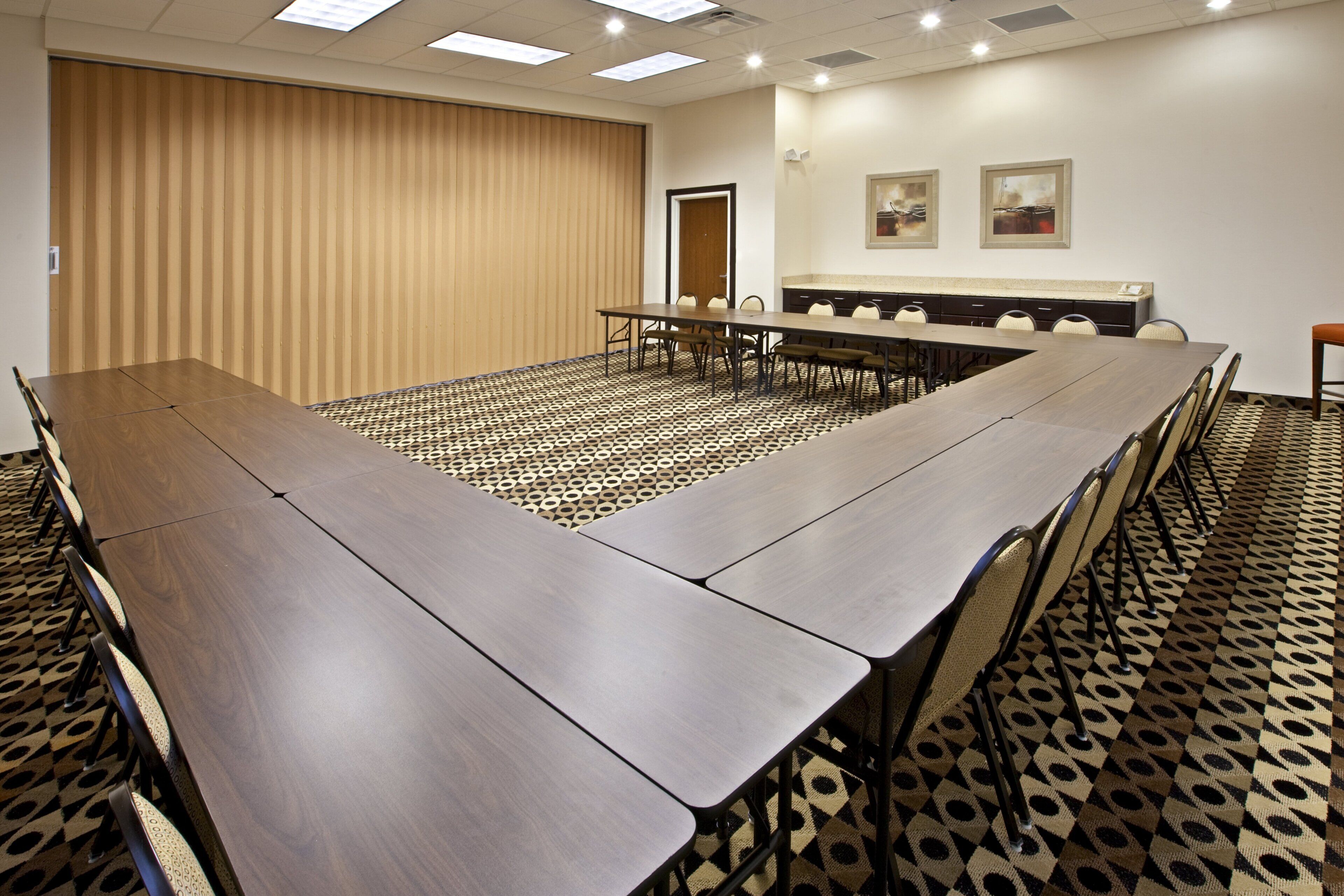 Un salón de conferencias con una larga mesa, sillas, una alfombra estampada y una puerta.
