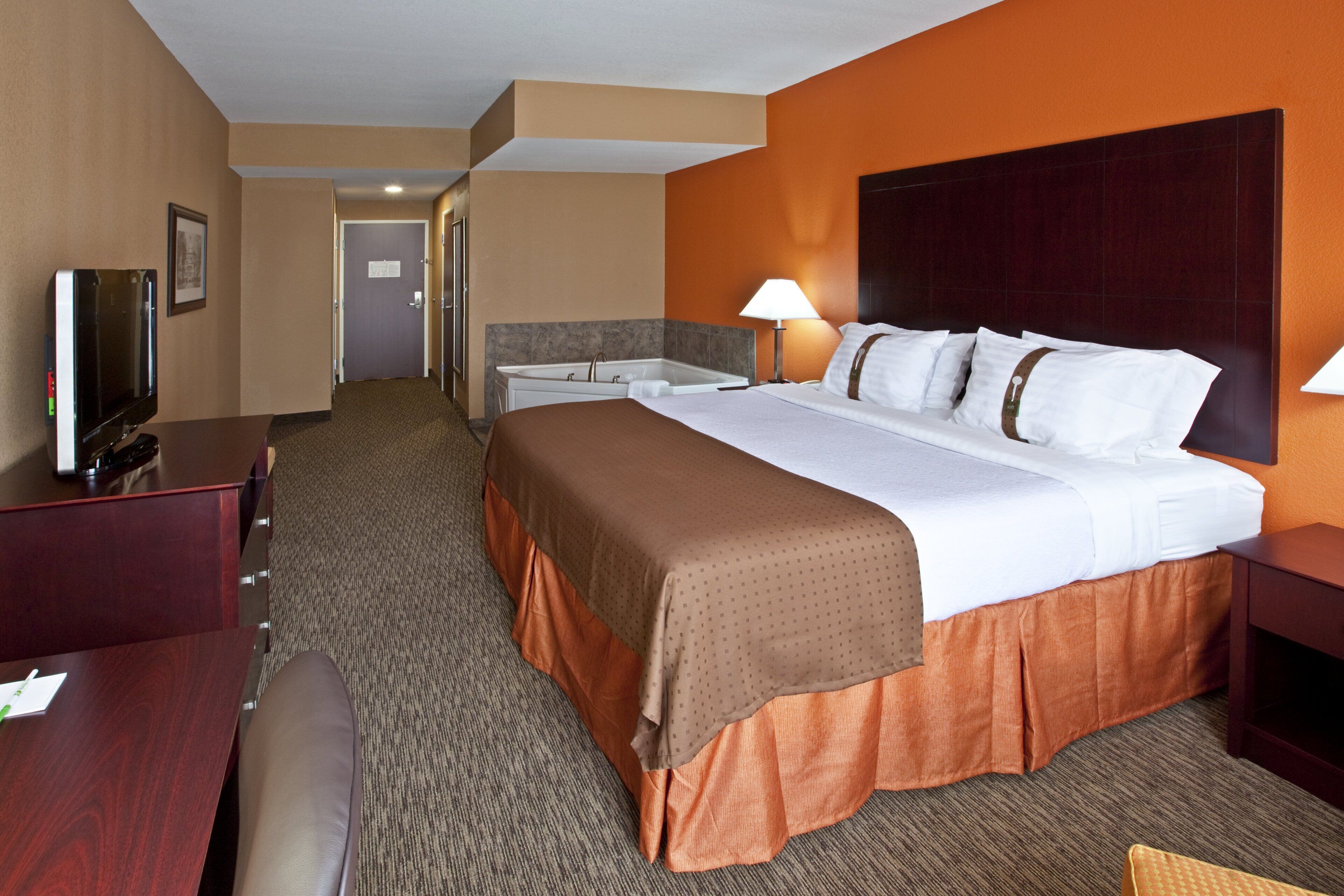 A hotel room with a bed, bedside tables, a TV, and a bathroom.