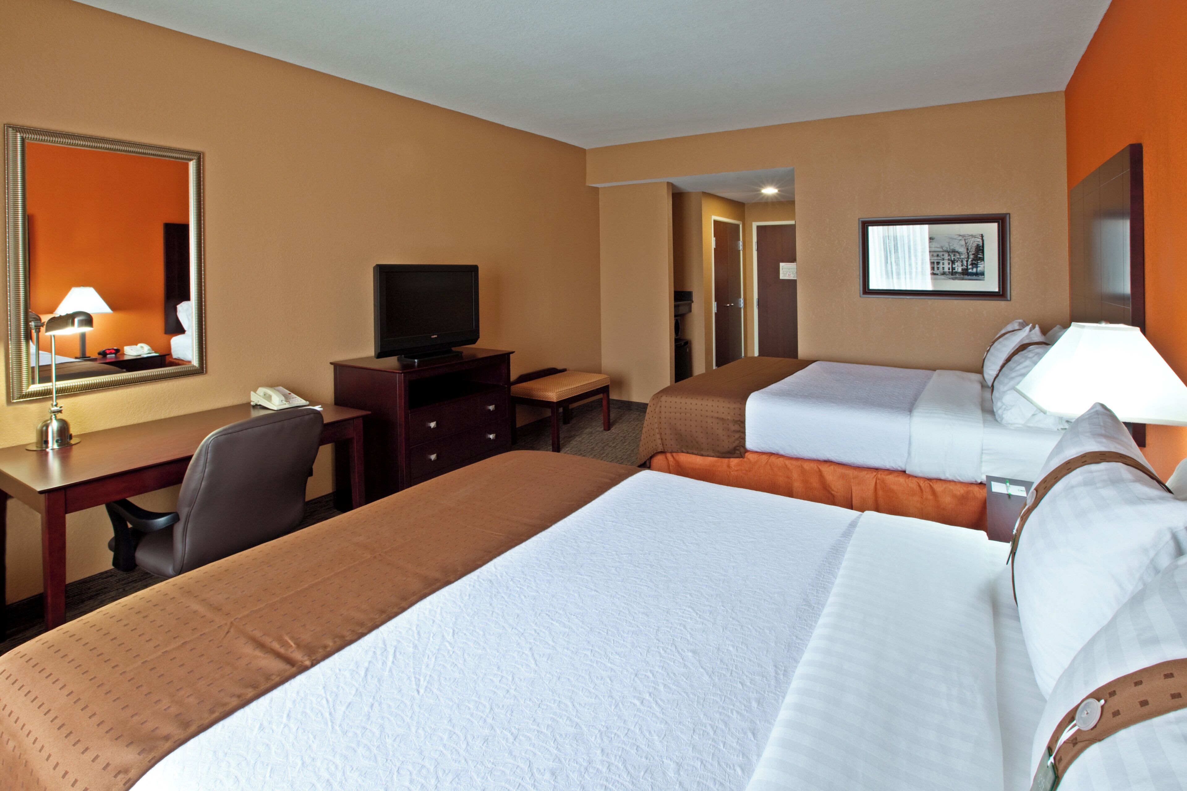 A hotel room with two beds, a desk, a television, and a mirror.