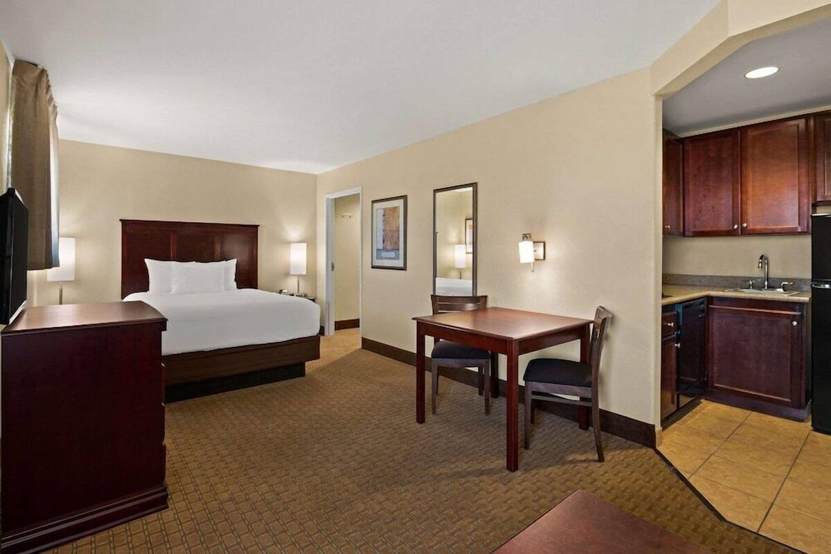 Ein Hotelzimmer mit Bett, Schreibtisch, Stuhl, Spiegel, Kommode und einer Küchenzeile.