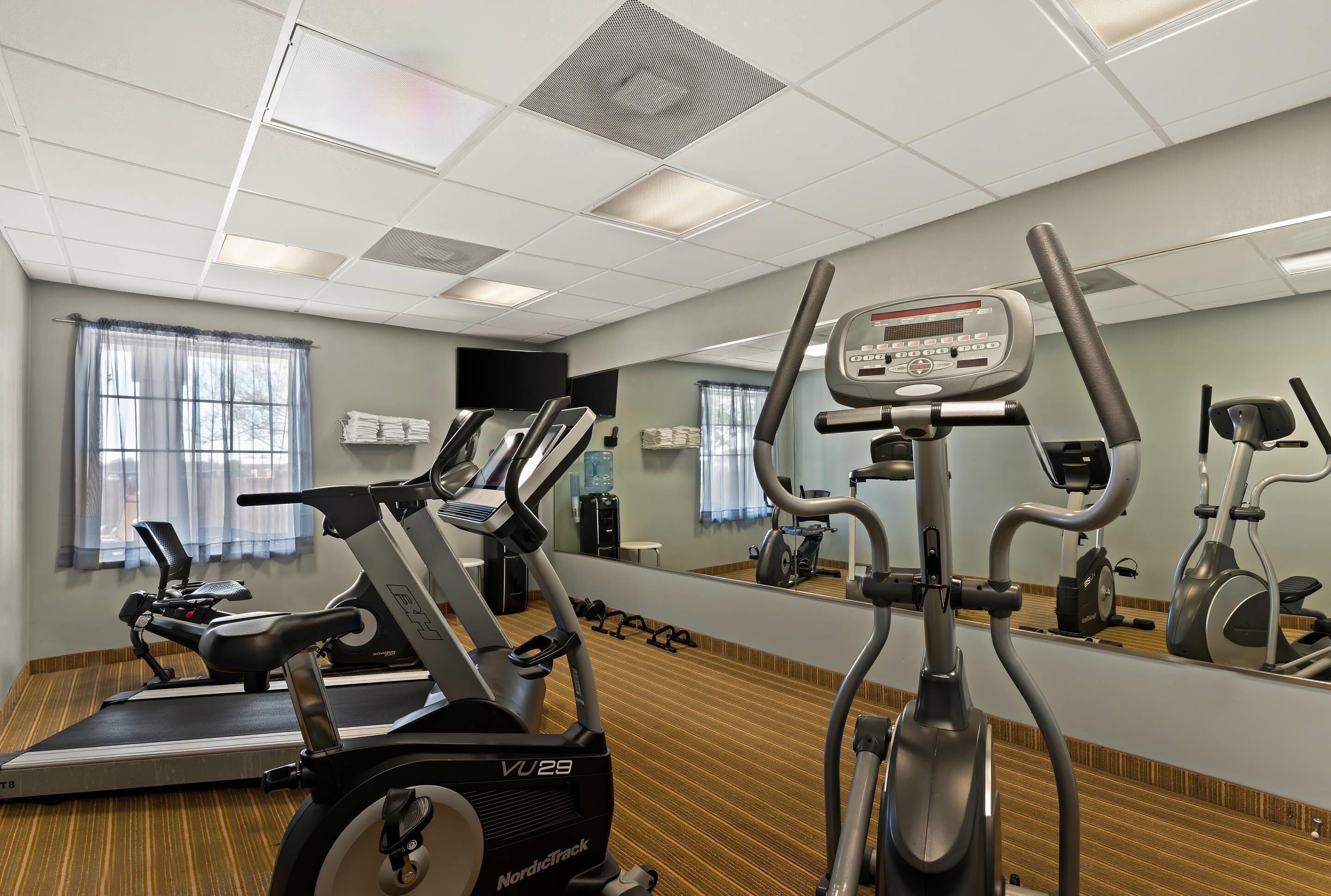 A gym with various exercise equipment, including treadmills and stationary bikes, and a large mirror reflecting the space.